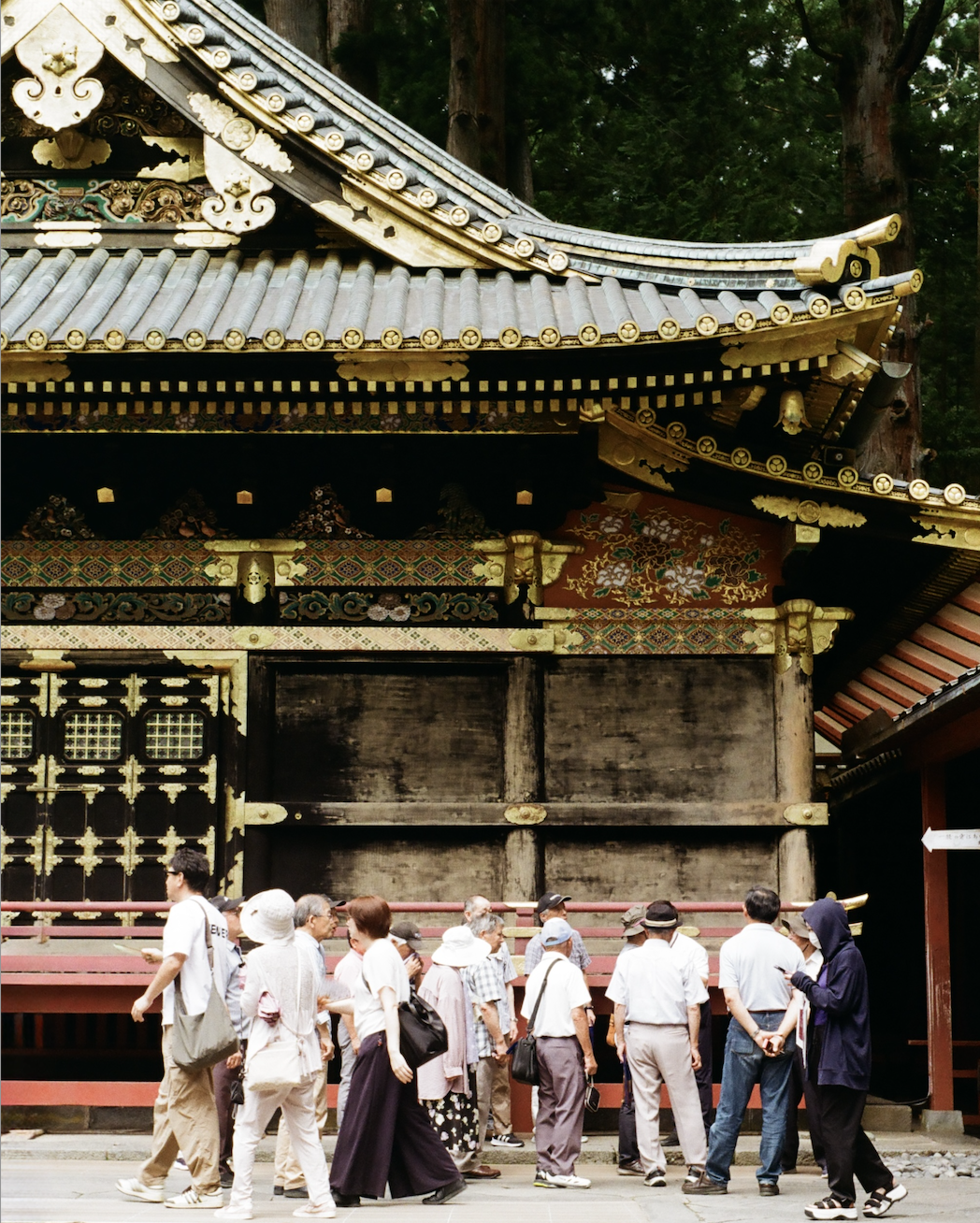 Group of people walking and standing in front of a traditional Japanese temple with ornate gold and wooden architectural details.