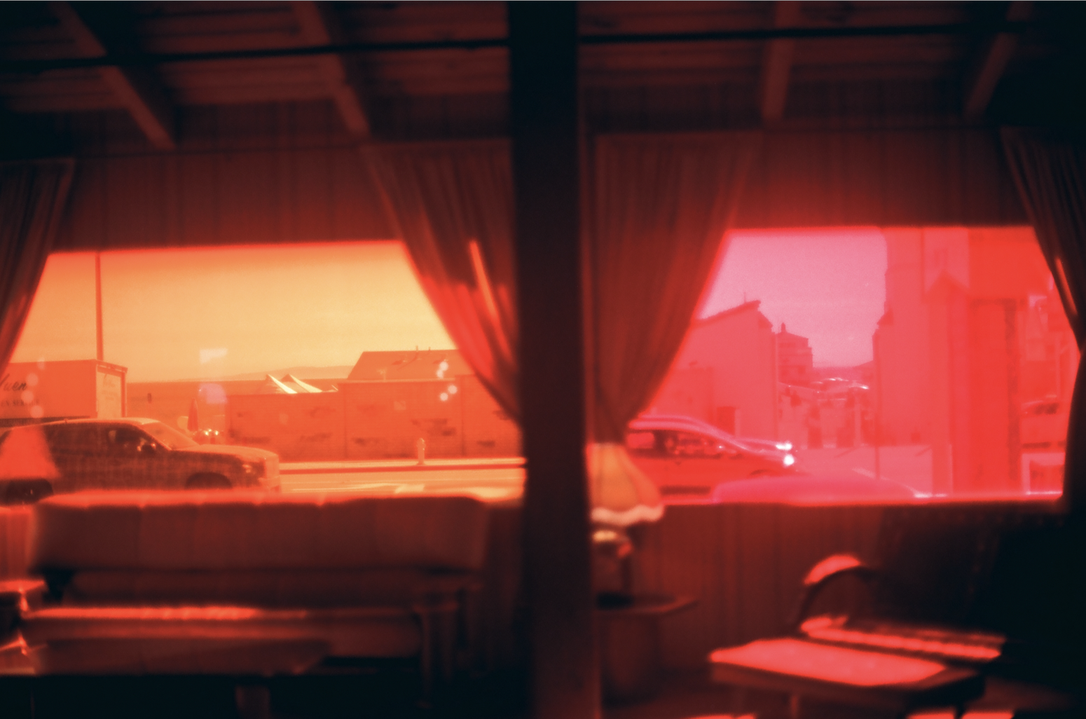 Interior of a room with a sofa, table, and lamp, viewed through red-tinted windows showing cars and buildings outside.